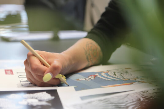 Hand einer Person, welche auf ein Blatt Papier zeichnet.