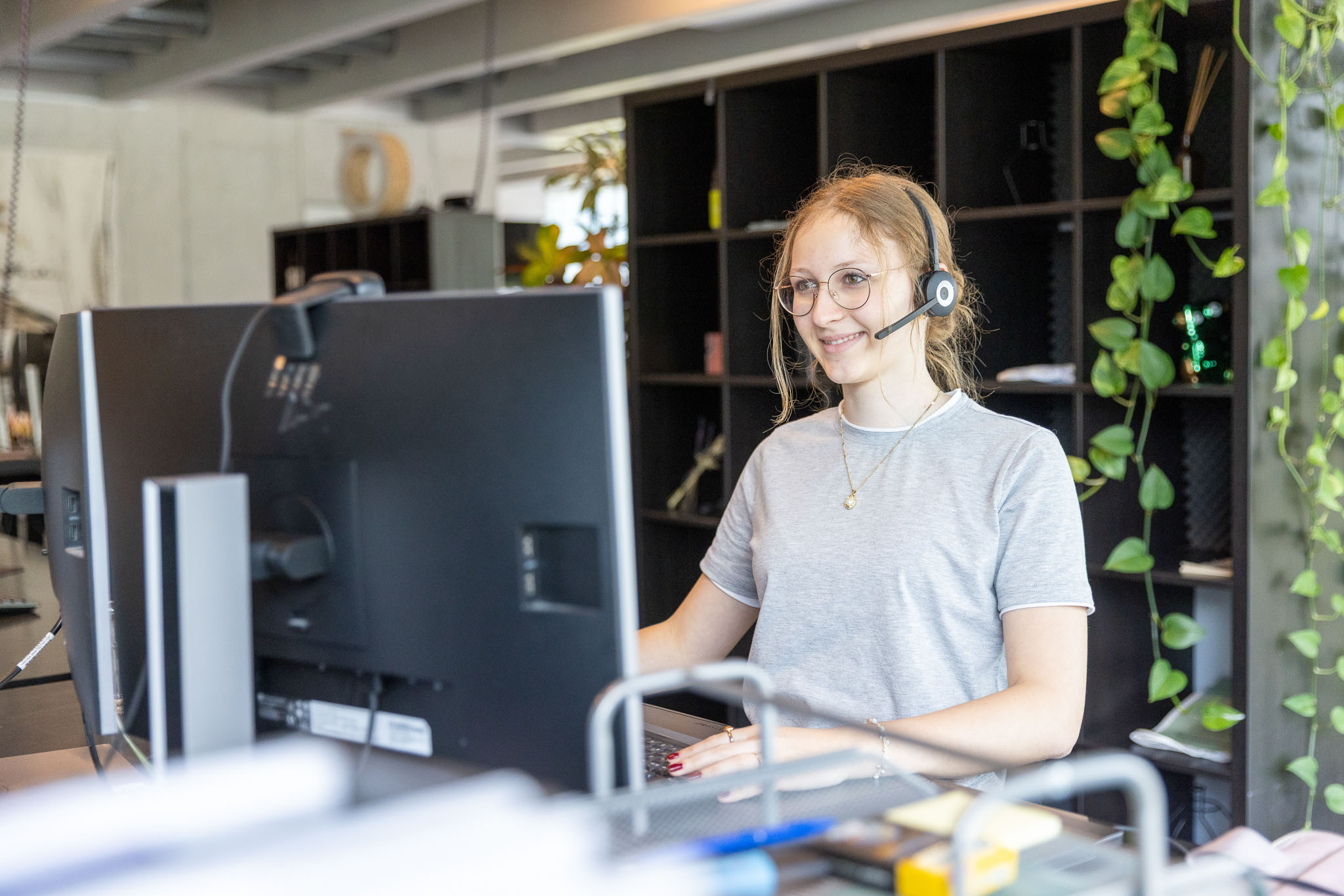 Lernende Lehrtochter mit Headset am Computer in einem modernen Büro. Symbolbild für Kundenservice, Support, Kommunikation, digitale Dienstleistungen und Teamarbeit.