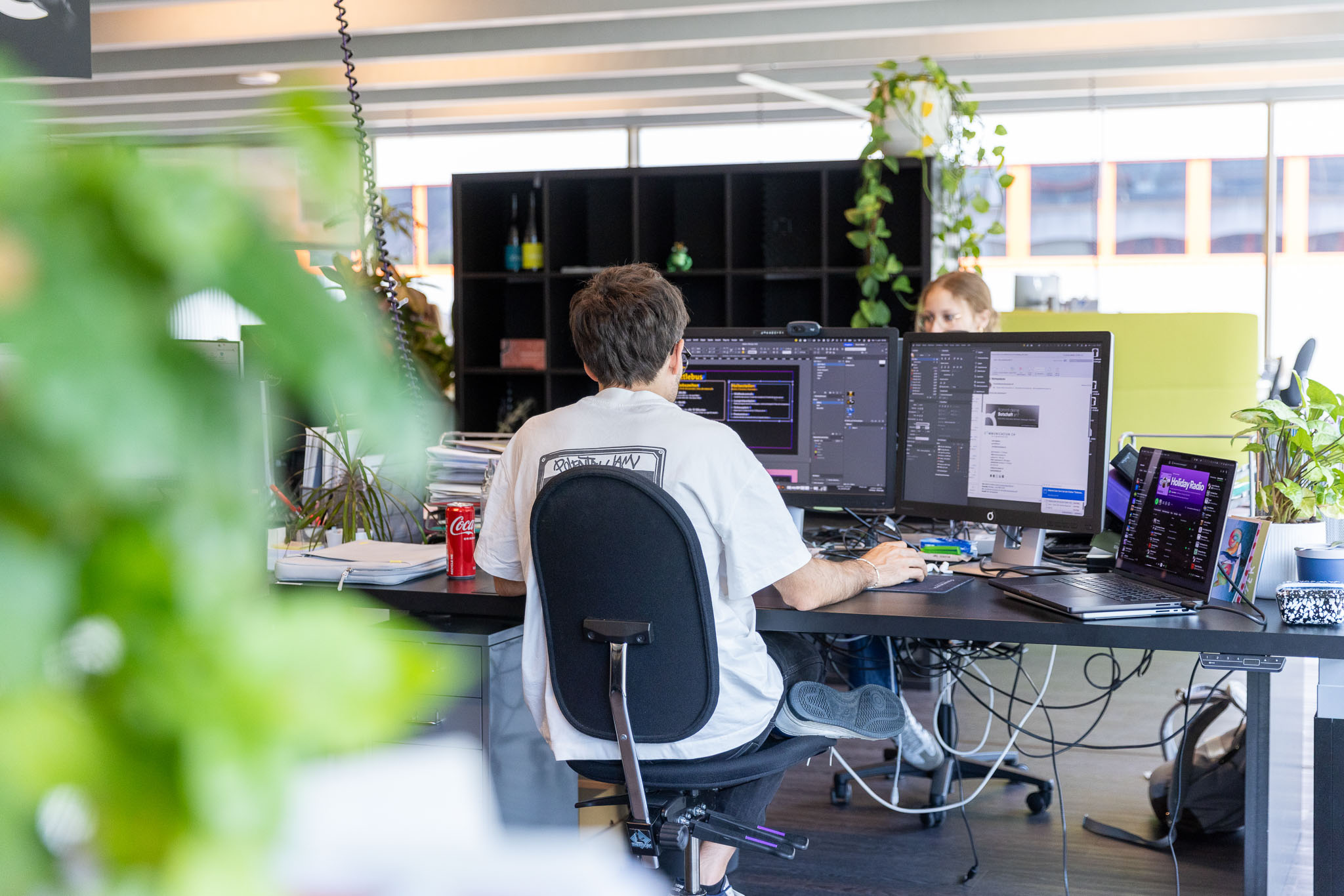 Grafikdesigner arbeitet an mehreren Bildschirmen in einem modernen Büro. Symbolbild für Webdesign, Grafikdesign, Medienproduktion, digitale Kommunikation und kreative Dienstleistungen.