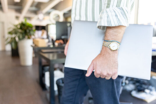 Person mit Laptop in modernem Bürogebäude, unterwegs zwischen Arbeitsplätzen. Symbolbild für Projektmanagement, Digitalisierung, Beratung und Büroarbeit.